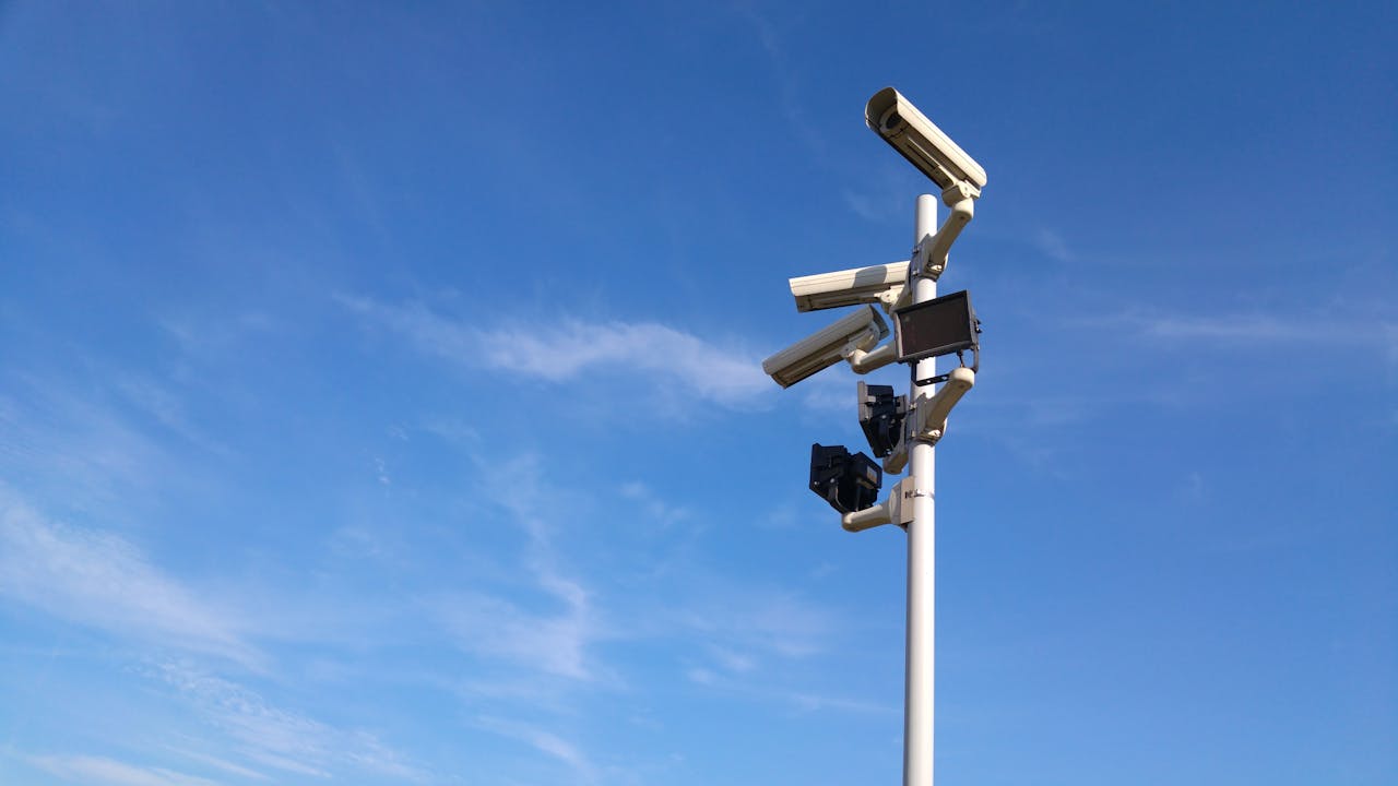 services-01 Multiple security cameras on a pole with a clear blue sky backdrop.